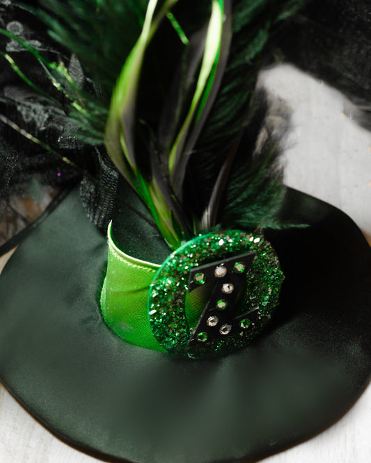 Green feathered  mini witch hat with a green ribbon and embellishments on a black background